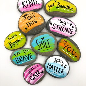 May include: Ten painted rocks with inspirational messages, including "be kind", "you got this", "stay strong", "be brave", "you can", "you matter", "have hope", "just breathe", "be you", and "smile".