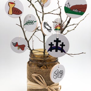 May include: A white branch with nine round white ornaments hanging from it. Each ornament has a different black and white illustration depicting a scene from the Easter story. The branch is in a brown glass jar with a burlap covering and a brown ribbon.