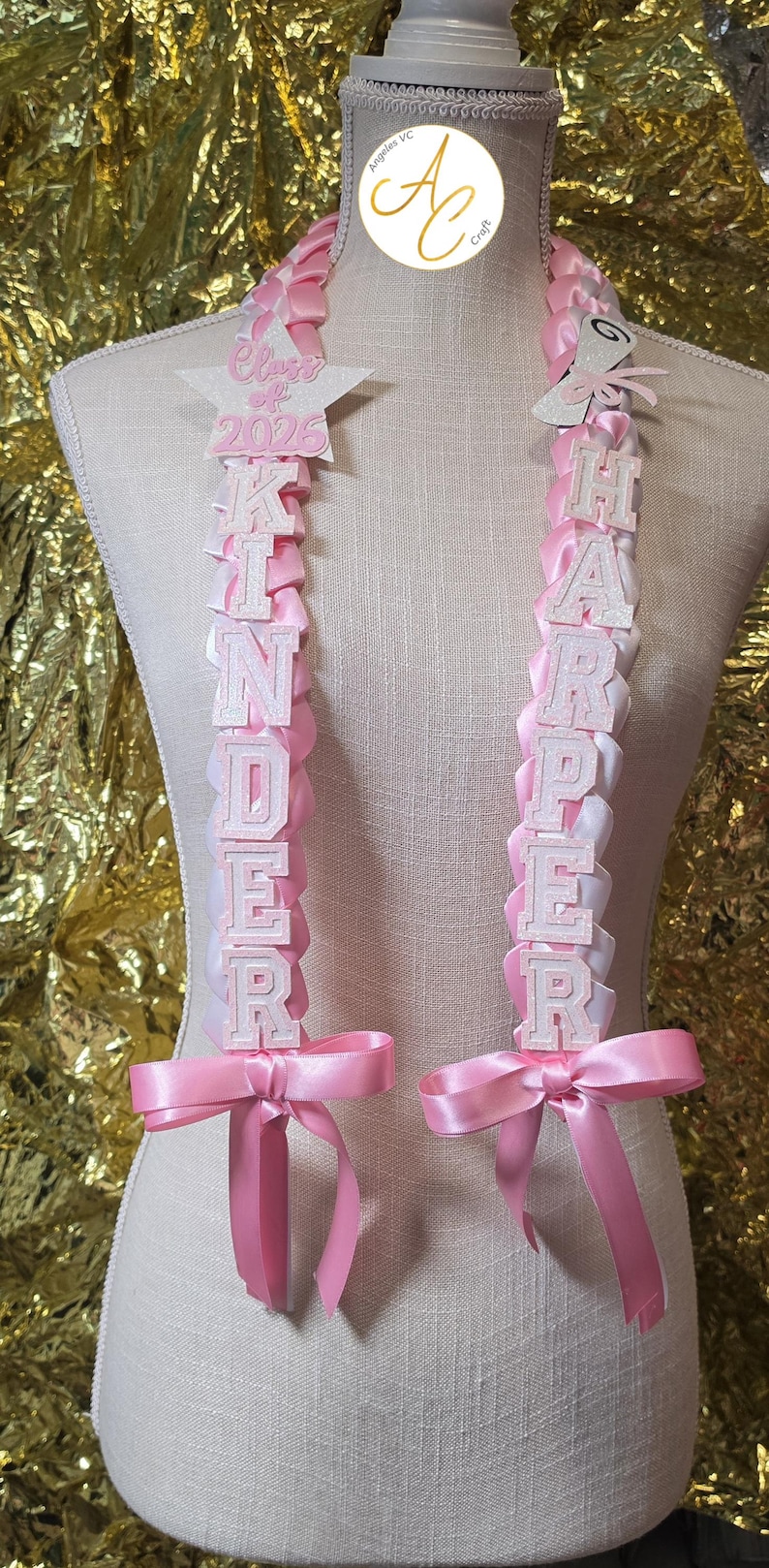 K&ouml;nnte beinhalten: Rosa-wei&szlig;e Abschlussleis mit den Namen "Kinder" und "Harper" in wei&szlig;en Buchstaben geschrieben. Jede Lei hat eine rosa Schleife unten und einen Stern mit "Klasse von 2025" oben.