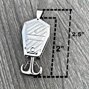 Op de afbeelding: Een zilveren metalen hanger in de vorm van een kist met een haak aan de onderkant. De hanger is 5 cm breed en 6,35 cm hoog.