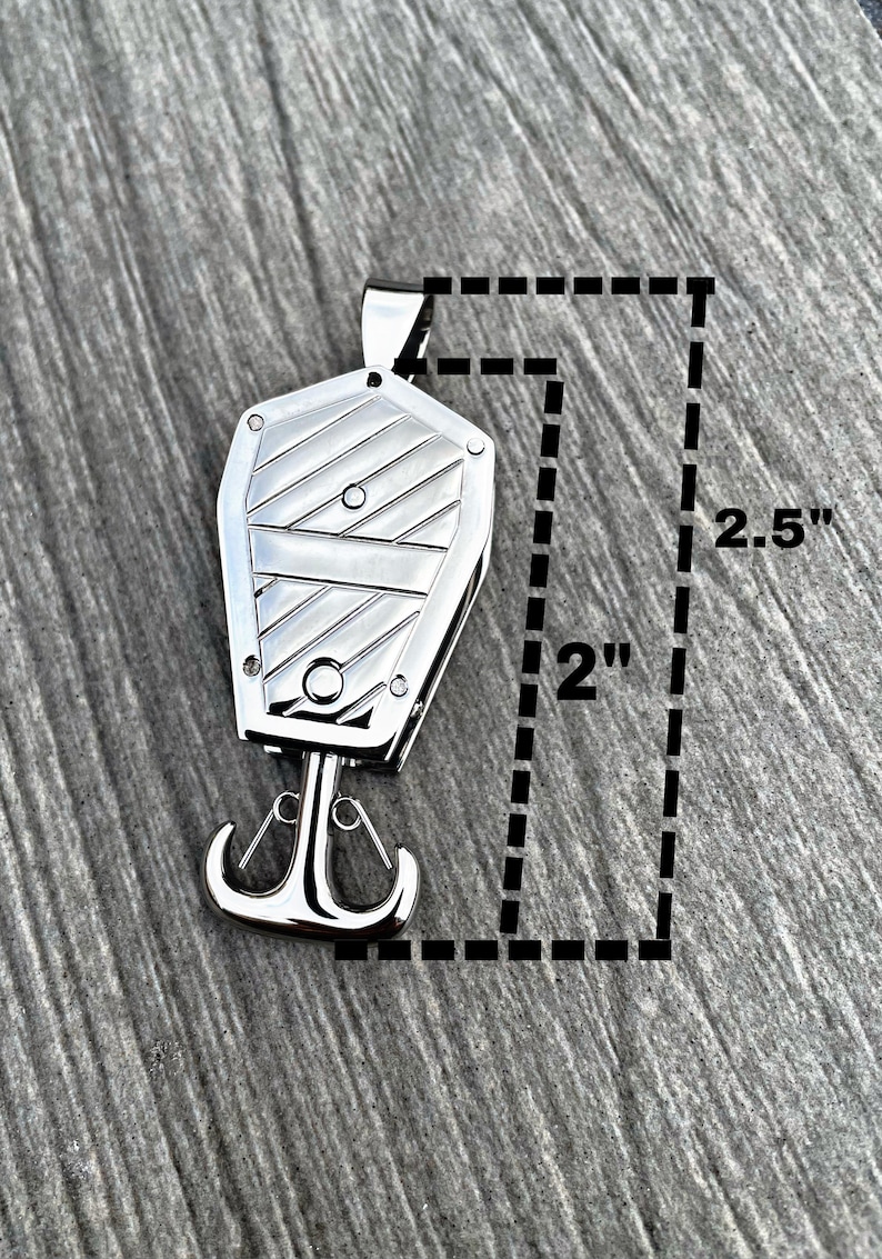 Op de afbeelding: Een zilveren metalen hanger in de vorm van een kist met een haak aan de onderkant. De hanger is 5 cm breed en 6,35 cm hoog.