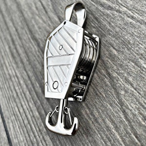 May include: A silver metal keychain with a detailed anchor design and a rope-like winding mechanism. The keychain is shaped like a coffin.