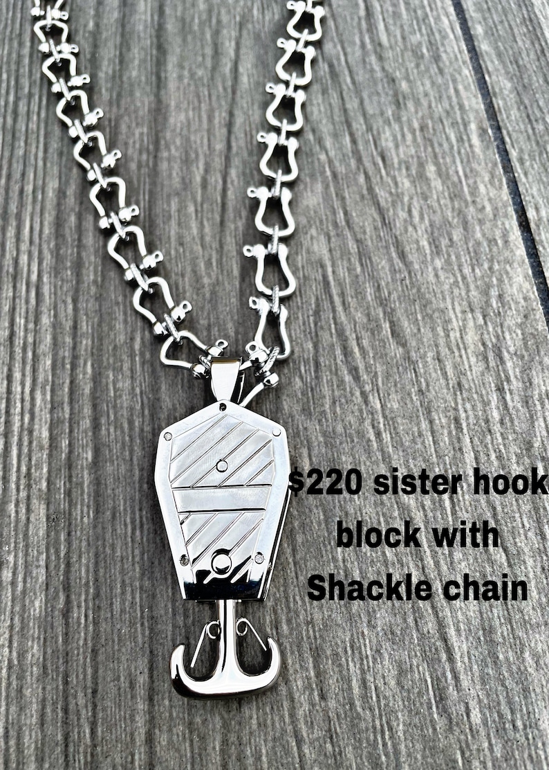 Op de afbeelding: Zilveren zusterhaak-blokanhanger met een zilveren shackle-ketting. De hanger heeft een getextureerd oppervlak en een haak aan de onderkant. De tekst "$220 sister hook block with Shackle chain" is zichtbaar in de afbeelding.
