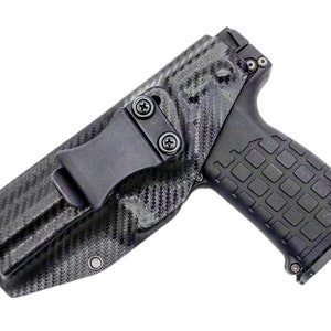 May include: A black carbon fibre holster with a clip for a handgun. The holster has a textured design and a black finish.