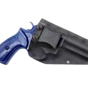 May include: A black leather holster with a blue handgun inside. The holster has a metal clip for attaching to a belt.