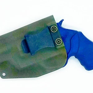 Op de afbeelding: Een blauwe en zwarte pistoolholster met een clip. De holster is gemaakt van camouflage stof en heeft een metalen ring aan de zijkant.