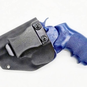 Op de afbeelding: Een zwart leren holster met een clip om een ​​blauwe revolver te dragen. De revolver heeft een zwarte greep en een zilveren loop.