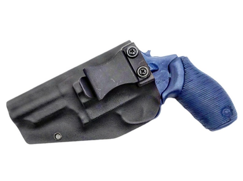 K&ouml;nnte beinhalten: Ein schwarzes Lederholster mit einem Clip zum Tragen eines blauen Revolvers.