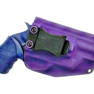 Op de afbeelding: Een paarse en blauwe pistoolholster met een zwarte clip. De holster is gemaakt van een getextureerd materiaal en heeft een metalen lus aan de zijkant.