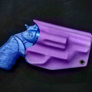Op de afbeelding: Een paarse leren holster voor een klein pistool. De holster heeft een gestructureerd ontwerp en een klein gaatje aan de zijkant.
