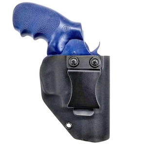 Puede incluir: Un revólver azul con empuñadura texturizada está parcialmente insertado en una funda negra moldeada. La funda cuenta con un clip de cinturón de metal negro asegurado por dos tornillos y un ojal en el borde inferior para sujetar el arma.