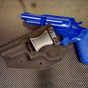 K&ouml;nnte beinhalten: Eine blaue Pistole mit einem schwarzen Holster. Das Holster hat einen Metallclip.