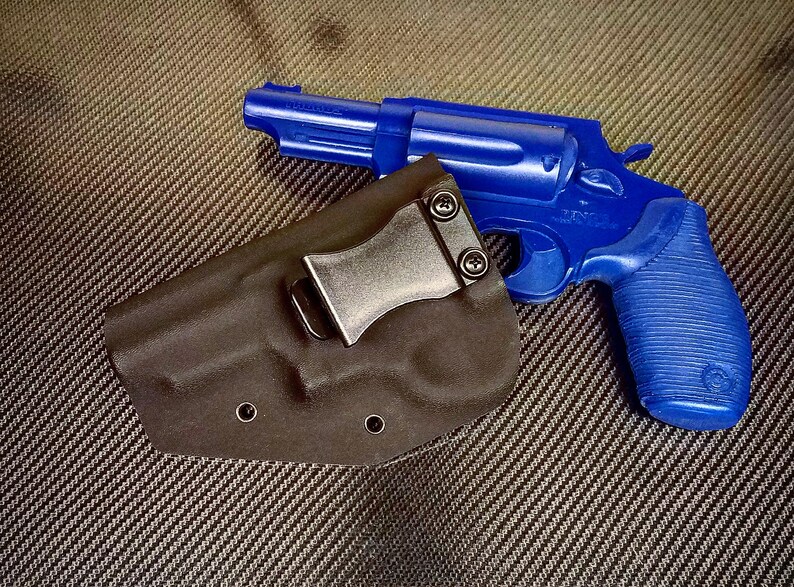 K&ouml;nnte beinhalten: Eine blaue Pistole mit einem schwarzen Holster. Das Holster hat einen Metallclip.