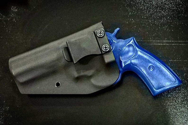 May include: A black leather holster with a clip for a blue handgun. The holster has a single hole on the side.