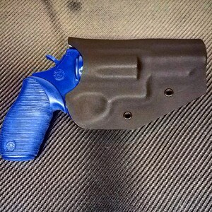 K&ouml;nnte beinhalten: Ein blauer Revolver mit einem schwarzen Lederholster. Das Holster hat zwei Druckkn&ouml;pfe.