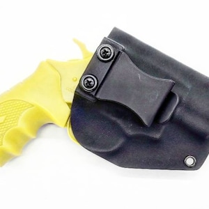 Könnte beinhalten: Ein schwarzes Lederholster mit einem Clip zum Tragen einer kleinen gelben Pistole.