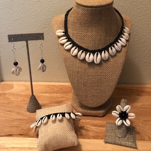May include: A set of jewellery made with white seashells and black cord. The set includes a necklace, a bracelet, a ring, and a pair of earrings.