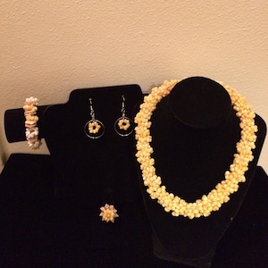 May include: A set of yellow shell jewelry, including a necklace, earrings, bracelet, and ring. The jewelry is displayed on a black velvet stand.