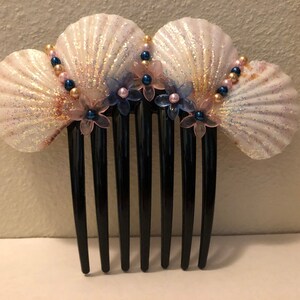 Puede incluir: Un peine para el cabello de concha blanca y dorada con flores rosas y azules y perlas.