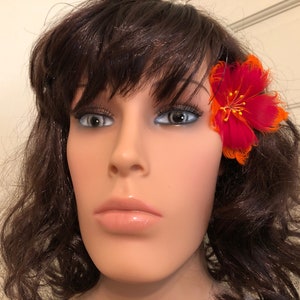 May include: A red and orange feather flower hair clip. The flower is approximately 5 cm in diameter and has a single yellow centre.