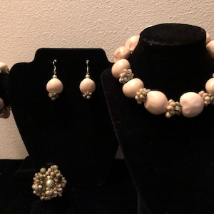 May include: A set of jewelry made from natural materials. The set includes a necklace, bracelet, earrings, and a ring. The jewelry is made from light pink and white beads.