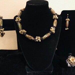 May include: A set of brown, green, and white agate bead jewelry. The set includes a necklace, bracelet, earrings, and a ring. The beads are all different shapes and sizes, and they are strung together with black thread.