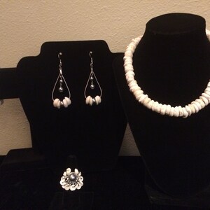 May include: A set of white shell jewellery featuring a necklace, bracelet, earrings, and a ring. The jewellery is accented with dark grey pearls.