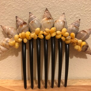 May include: A black hair comb with seven teeth decorated with seashells and yellow beads.
