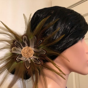 May include: A brown and green feather hair clip with a beige fabric flower in the center.