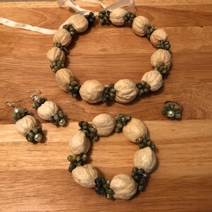 Könnte beinhalten: Ein Schmuckset aus natürlichen Materialien. Das Set beinhaltet eine Halskette, ein Armband, ein Paar Ohrringe und einen Ring. Der Schmuck ist aus beige und grünen Nüssen gefertigt und verfügt über kleine weiße Perlen.