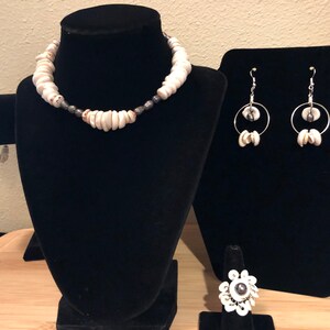 May include: A set of white shell jewelry, including a necklace, bracelet, earrings, and ring. The necklace and bracelet are made of white shell beads, while the earrings and ring feature a single white shell bead with a silver ring.