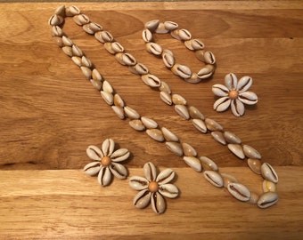Könnte beinhalten: Ein Schmuckset aus Muscheln mit einer langen Halskette, einem Armband und zwei Paar Ohrringen. Die Halskette und das Armband bestehen aus kleinen, weißen Muscheln, und die Ohrringe sind blumenförmig mit einem kleinen, orangefarbenen Zentrum.