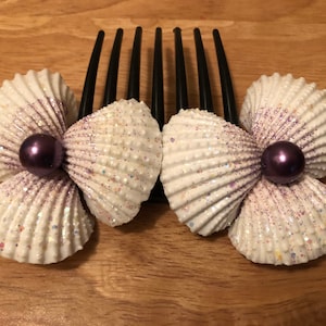 Puede incluir: Dos peines para el cabello de concha blanca con purpurina morada y una sola perla morada en el centro de cada peine.