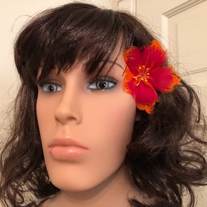 May include: A red and orange feather flower hair clip. The flower is made of feathers and has a red centre with orange petals.