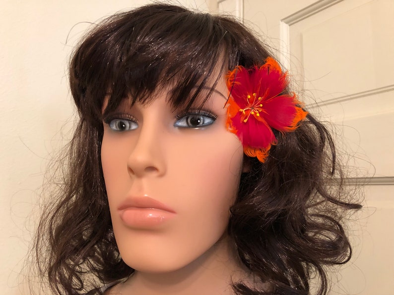 May include: A red and orange feather flower hair clip. The flower is made of feathers and has a red centre with orange petals.