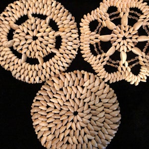 Può includere: Tre sottobicchieri circolari realizzati con piccole conchiglie bianche disposte a spirale. I sottobicchieri sono su uno sfondo nero.