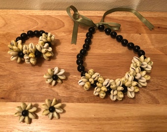 Könnte beinhalten: Ein Schmuckset mit einer Halskette, einem Armband und Ohrringen. Die Halskette und das Armband bestehen aus schwarzen Perlen und Kaurischnecken. Die Ohrringe bestehen aus Kaurischnecken und schwarzen Perlen.