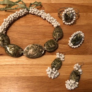 Könnte beinhalten: Ein Set aus grünem und weißem Muschelschmuck, bestehend aus einer Halskette, einem Armband und Ohrringen. Die Halskette und das Armband bestehen aus kleinen weißen Muscheln, die Ohrringe und das Armband haben größere grüne Muscheln in der Mitte.