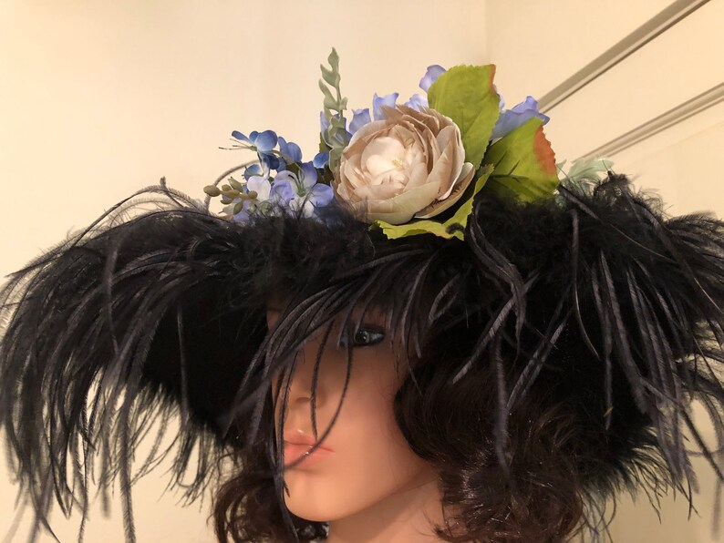 Pu&ograve; includere: Un cappello di piume nere con un grande fiore bianco e fiori blu in cima.