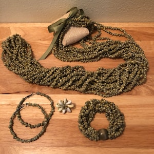 Könnte beinhalten: Ein Set aus grünen Muschelkette, einem Armband und einem Paar Ohrringen. Die Ketten sind aus kleinen, grünen Muscheln gefertigt und auf einer Schnur aufgereiht. Das Armband ist ebenfalls aus grünen Muscheln gefertigt und hat eine braune Perle in der Mitte. Die Ohrringe sind klein und rund und ebenfalls aus grünen Muscheln gefertigt.