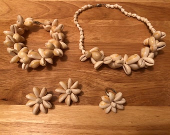 Könnte beinhalten: Ein Set aus Muschelschmuck, bestehend aus einer Halskette, einem Armband, Ohrringen und einem Ring. Der Schmuck ist aus natürlichen weißen Muscheln gefertigt und hat einen zarten, femininen Look.