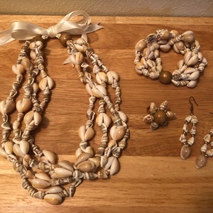 Op de afbeelding: Een set schelpensieraden, waaronder een ketting, armband, ring en oorbellen. De sieraden zijn gemaakt van natuurlijke schelpen in tinten wit en bruin.