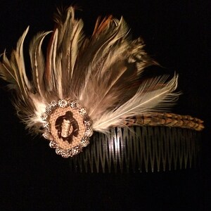 Puede incluir: Un peine para el cabello de plumas marrones y negras con un diseño de tortuga marrón y blanco. El peine está hecho de metal y tiene una fila de dientes.