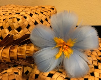 Può includere: Un cappello di paglia intrecciato con un fiocco di piume blu e giallo. Il cappello è fatto di materiali naturali e ha un aspetto rustico e fatto a mano.