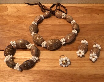 Könnte beinhalten: Ein Set aus braunem und weißem Muschelschmuck, bestehend aus einer Halskette, einem Armband, einem Ring und Ohrringen. Die Halskette und das Armband bestehen aus größeren Muscheln, während der Ring und die Ohrringe aus kleineren Muscheln bestehen.
