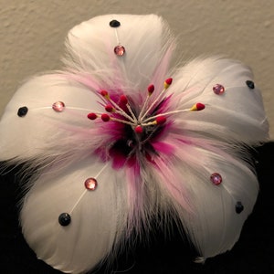 May include: A white feather flower with pink accents and black and pink rhinestones.