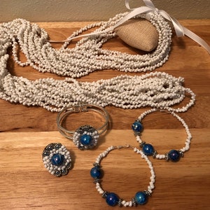 Könnte beinhalten: Ein Set aus weissen Perlen Schmuck mit blauen und silbernen Akzenten. Das Set beinhaltet eine lange Halskette, ein Armband, einen Ring und zwei Paar Ohrringe.