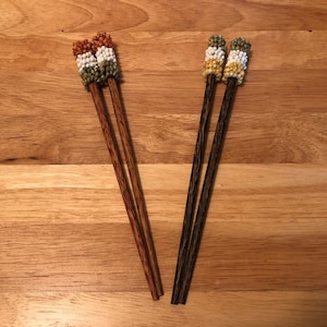 Peut inclure: Deux paires de baguettes avec des perles décoratives en haut. Une paire est brune et l'autre est noire. Les perles sont multicolores et comprennent du brun, du blanc et du vert.