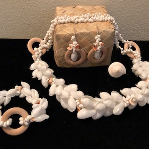May include: A set of white shell jewelry with wooden accents. The set includes a necklace, bracelet, and earrings. The necklace and bracelet are made of small white shells strung together with wooden beads. The earrings are made of larger white shells with wooden hoops.