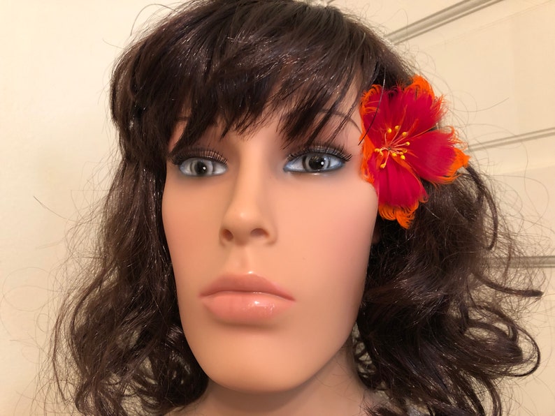 May include: A red and orange feather flower hair clip. The flower is approximately 5 cm in diameter and has a gold centre.